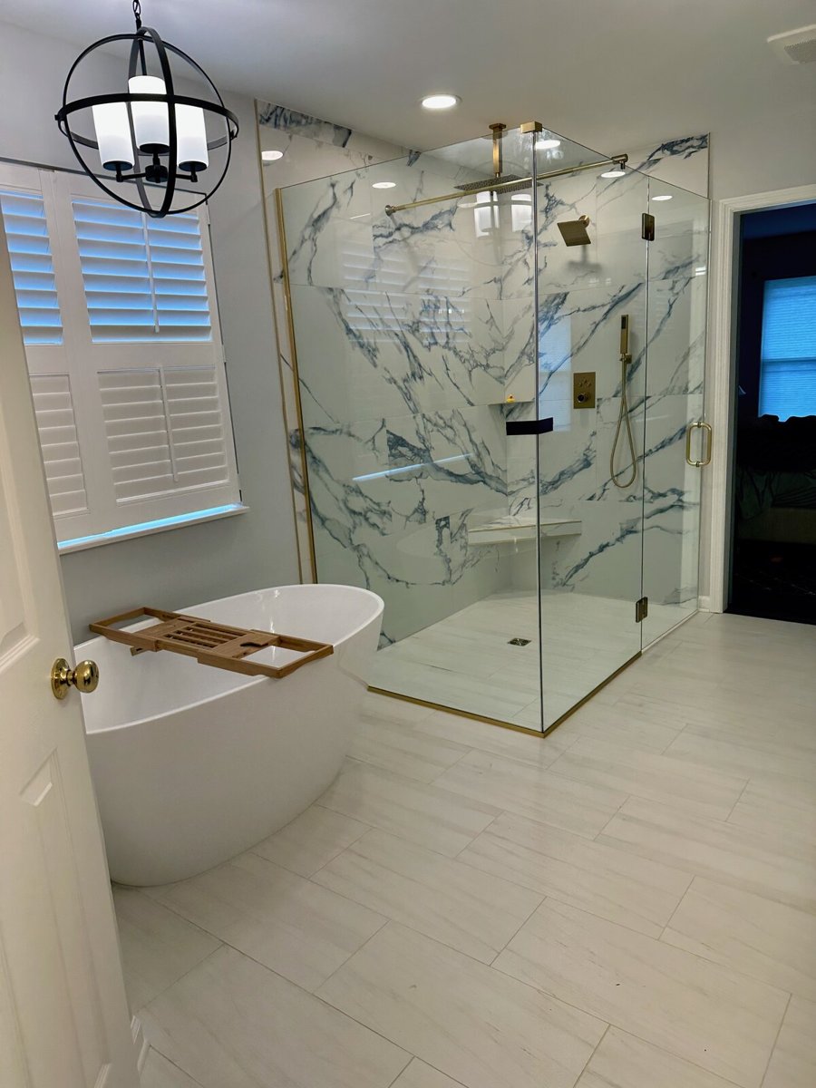 Bathroom after renovation, with a freestanding tub, glass shower, veined tile and brass fixtures